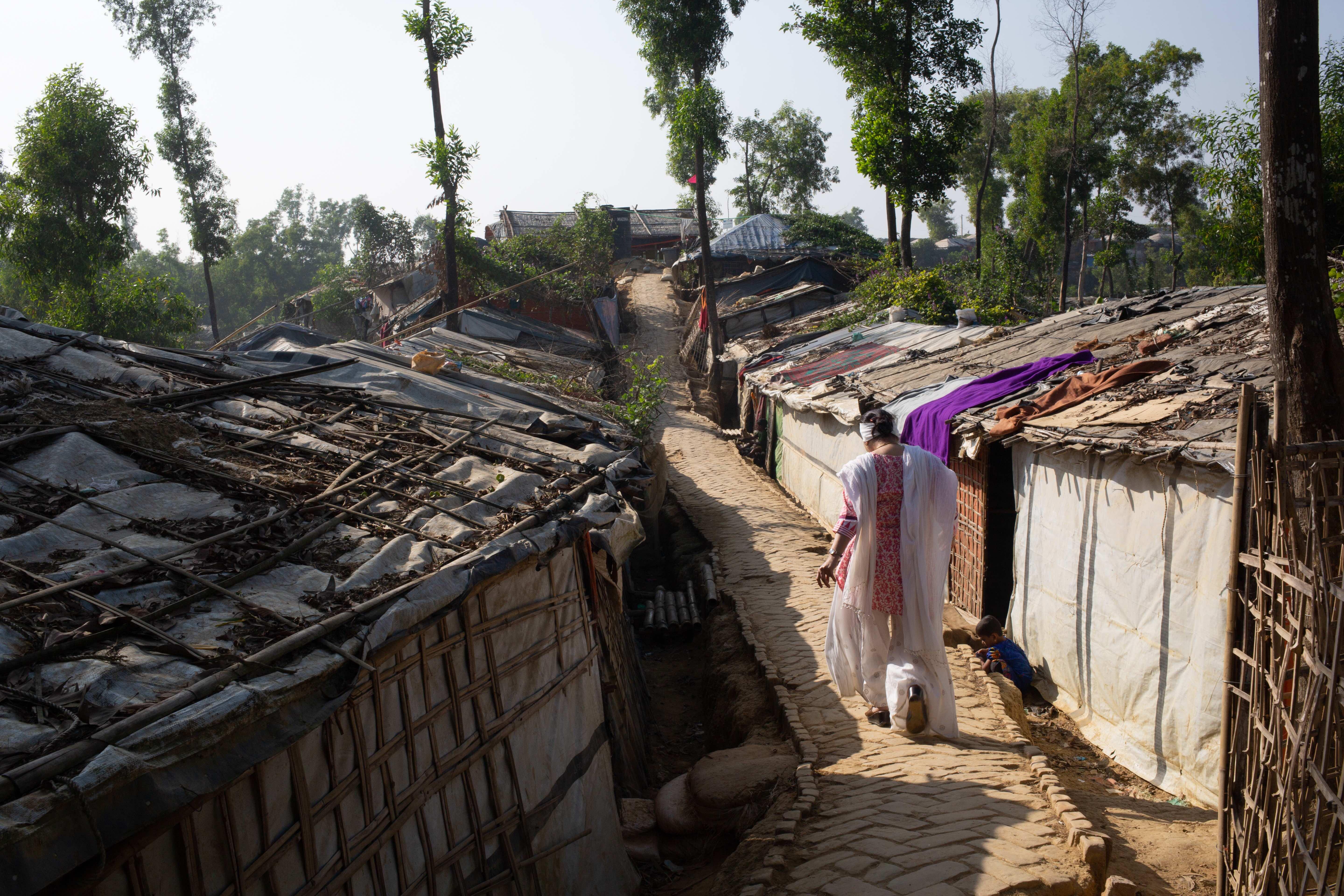 Razia Sultana walks in between a row of homes on a dust road