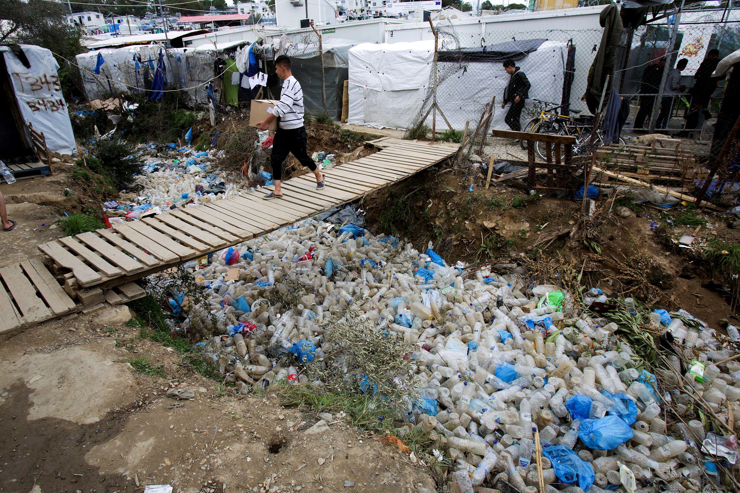 Man walking on wooden bridge under which are many discarded plastic bottles and rubbish