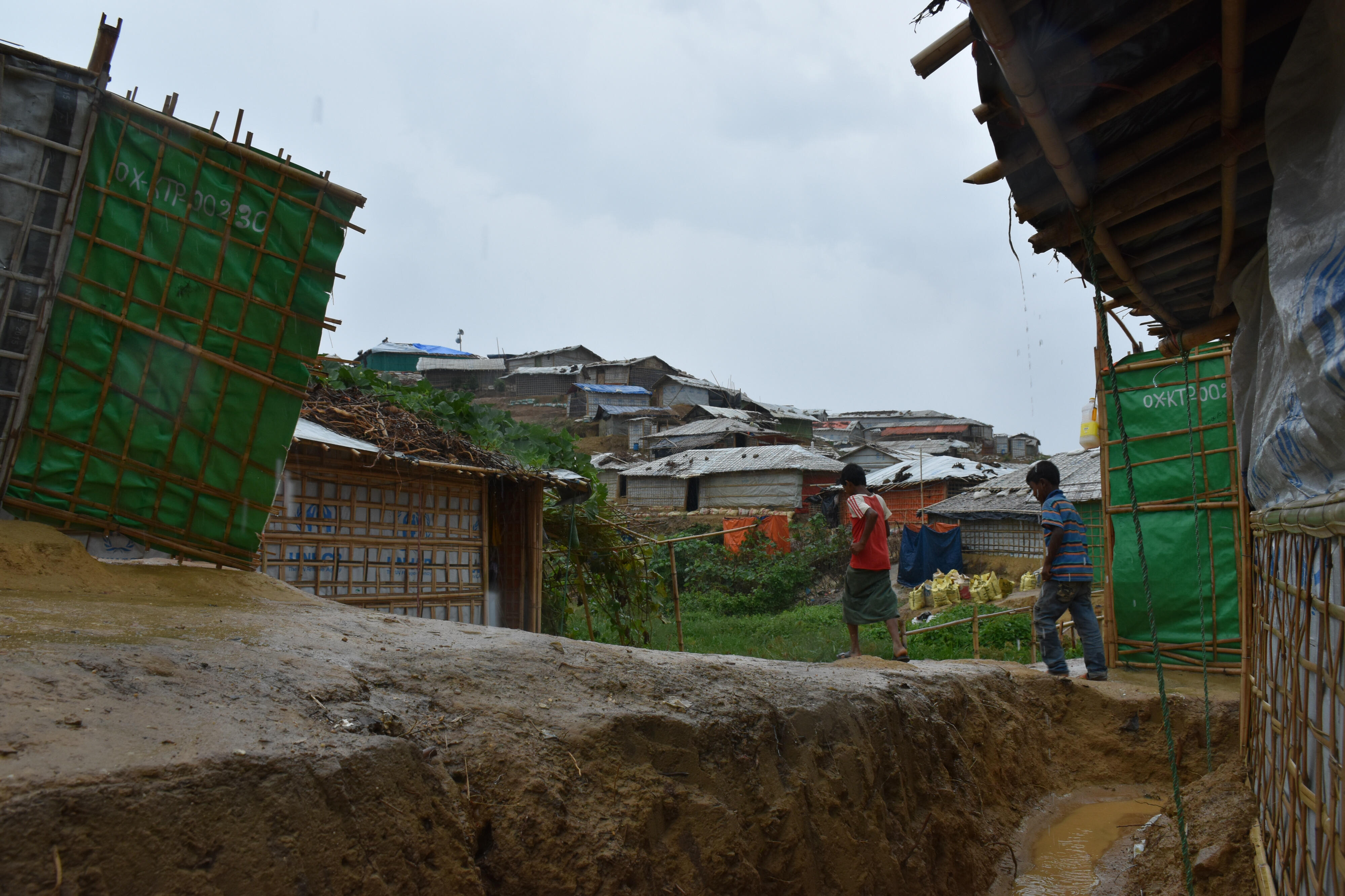 Two boys walk on muddy path through a refugee camp in Bangladesh