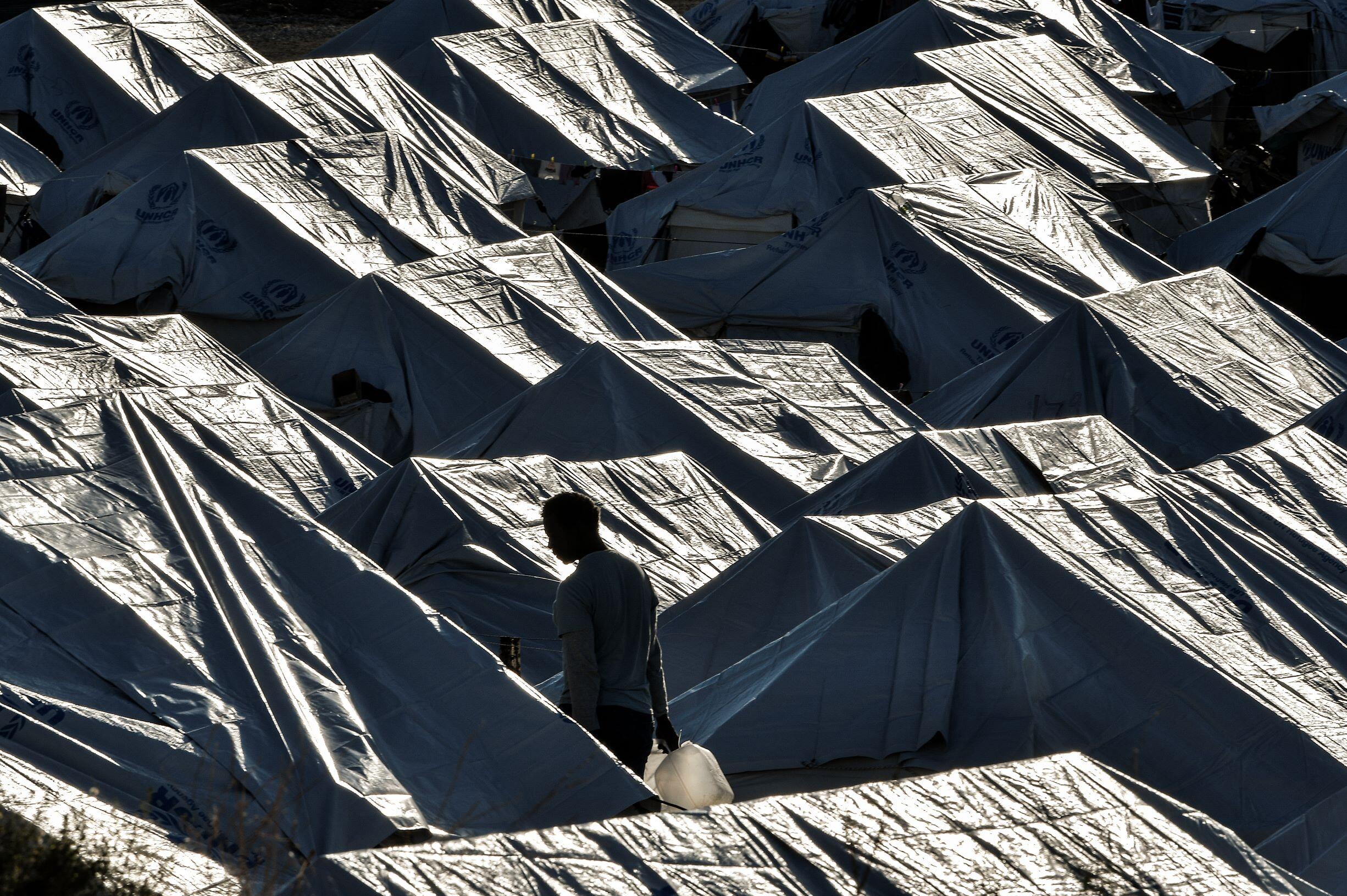 A man walks among tents with a water container 