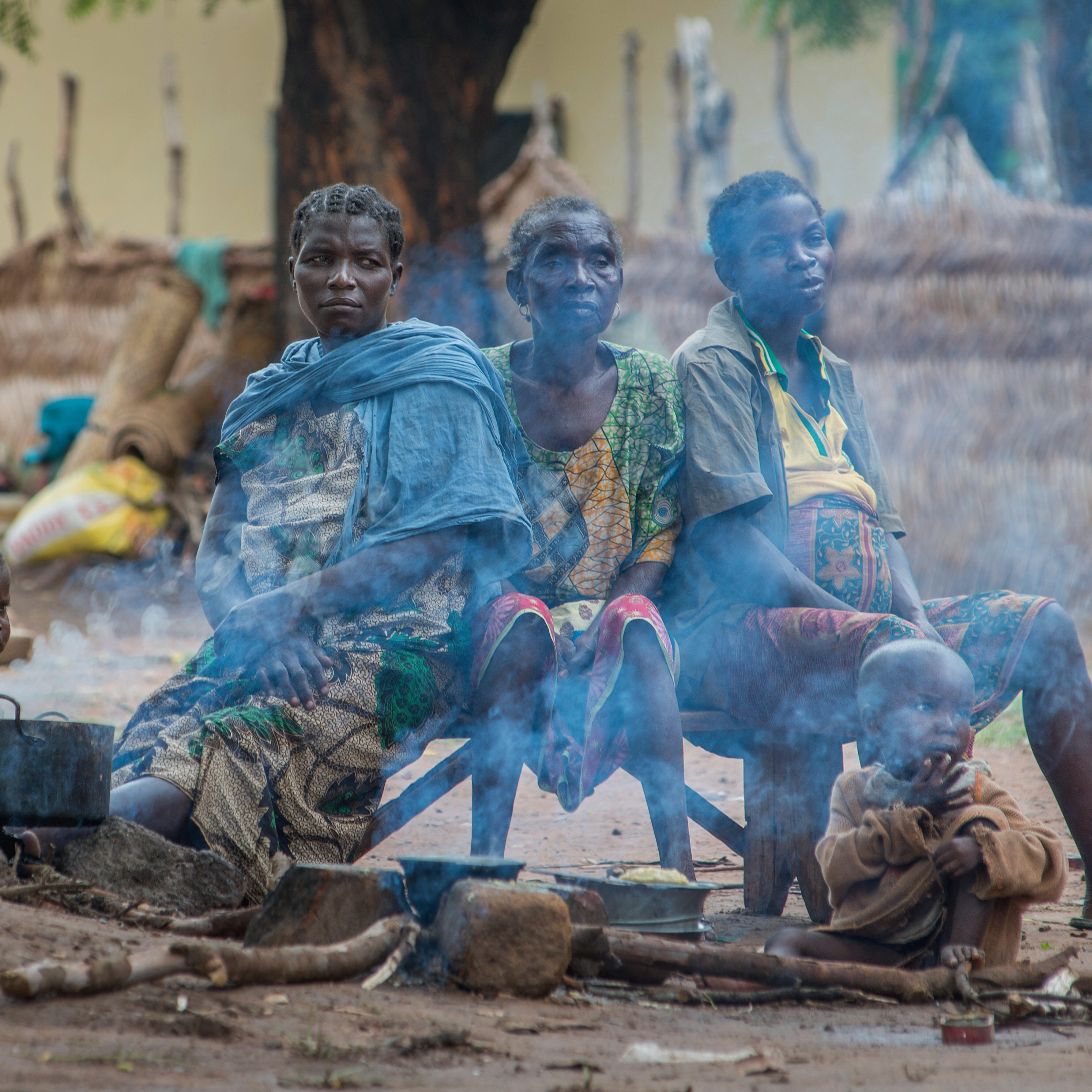 Three women and two children from CAR sit around a fireplace in a camp for displaced people.