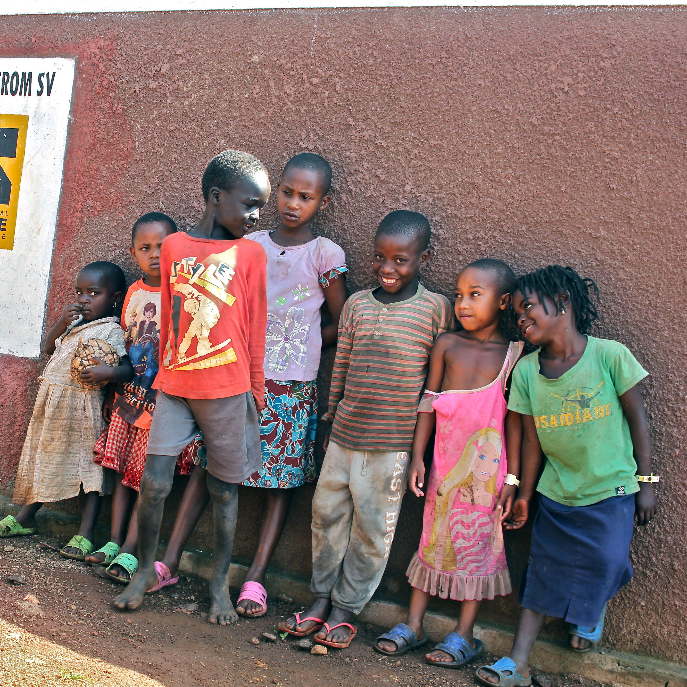 Children stand and pose for a picture in front of a red wall built by the IRC.