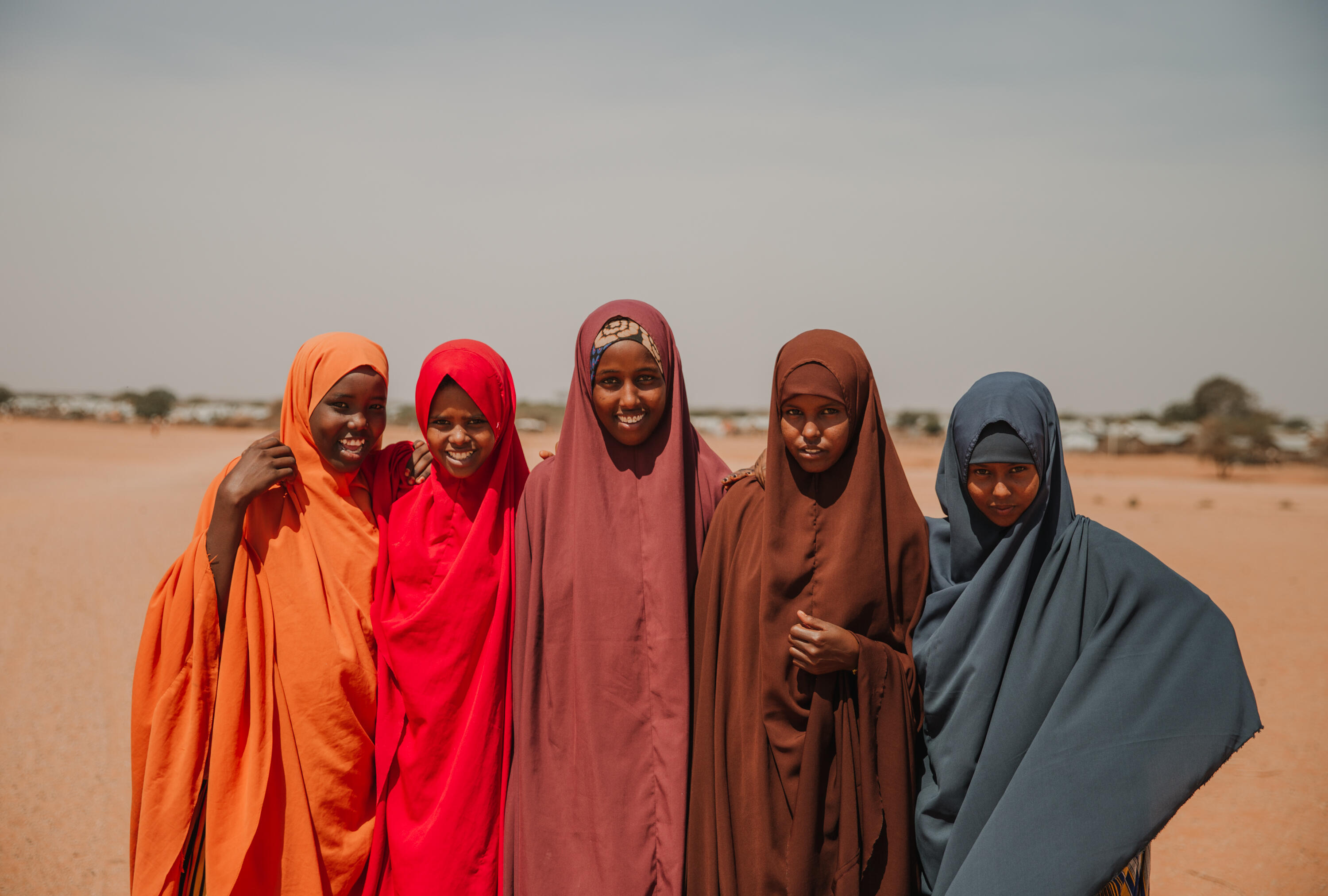 Five girls dressed in bright colours smile at the camera.