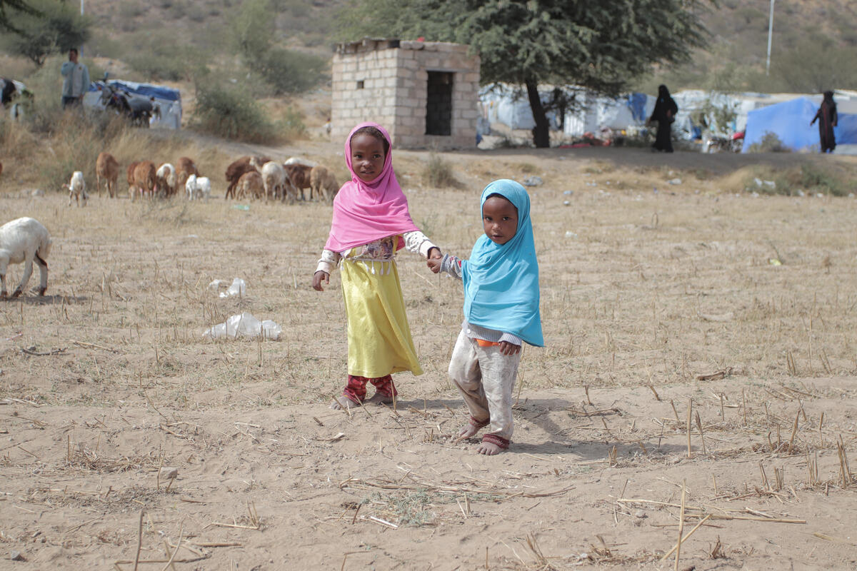 Two young girls hold hands in a dried out field in Yemen