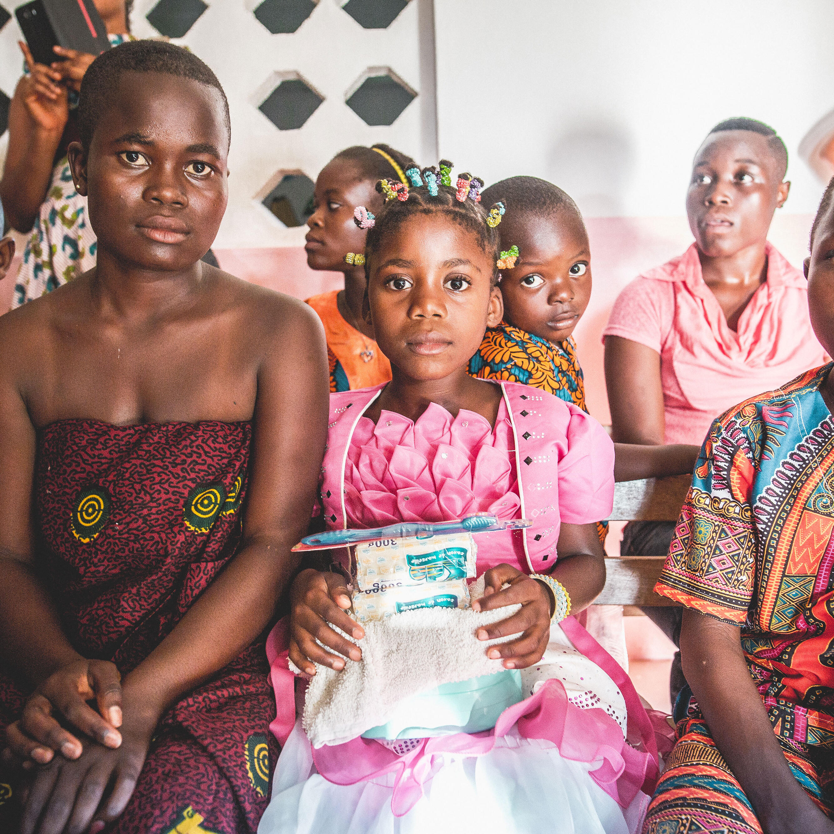 Women and children dressed festively sit at an indoors gathering in Ivory Coast.