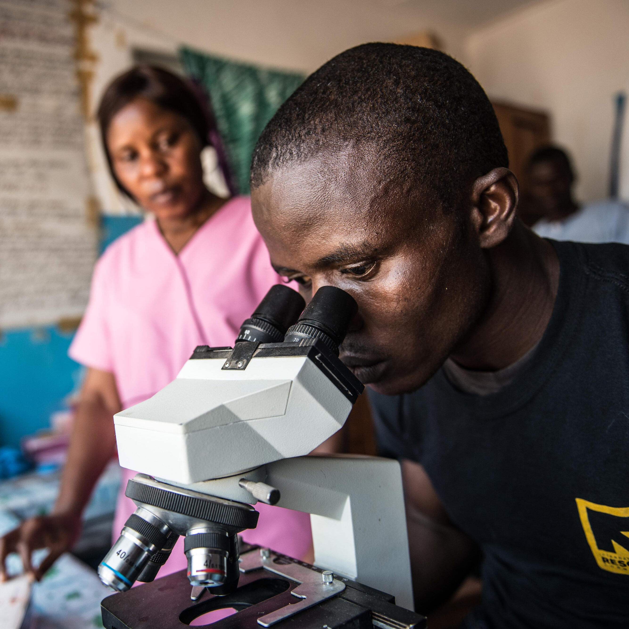 An IRC health worker testing for the Ebola virus examines a sample on slide on a microscope