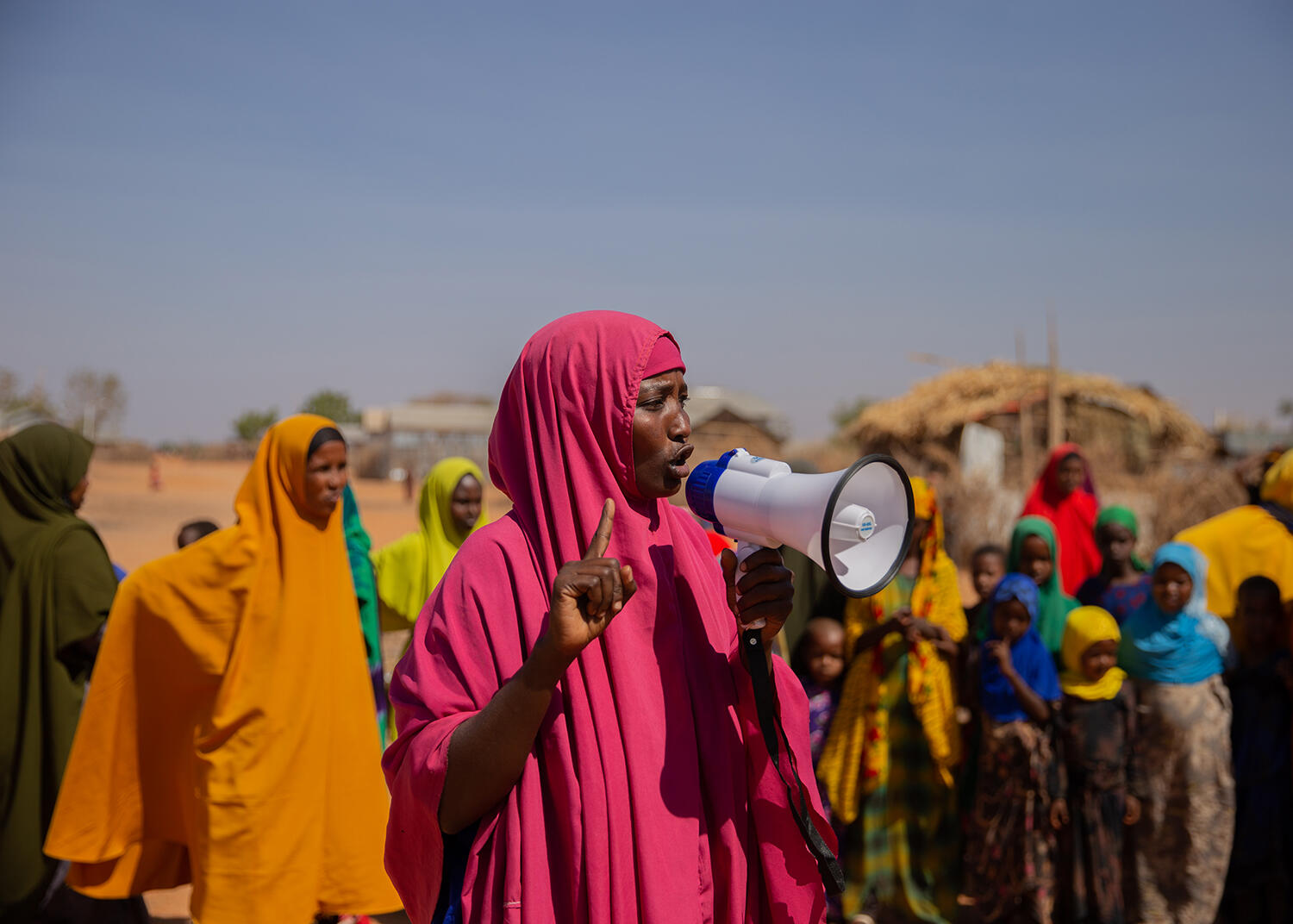 Zainab dressed in pink speaks into a megaphone in front of a crowd of people in Helowyn camp in Ethiopia. 