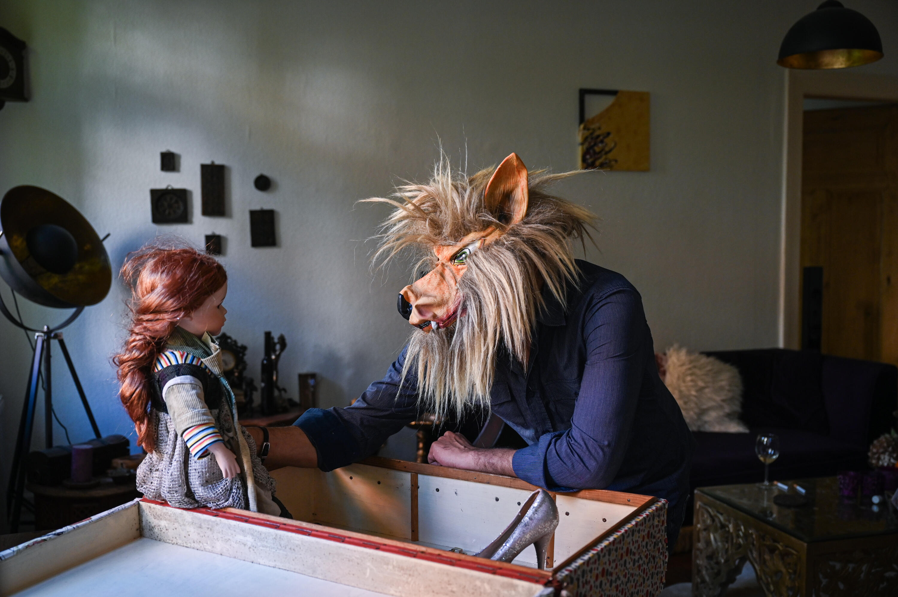 Bashar wearing a wolf mask and staring at a doll with red hair
