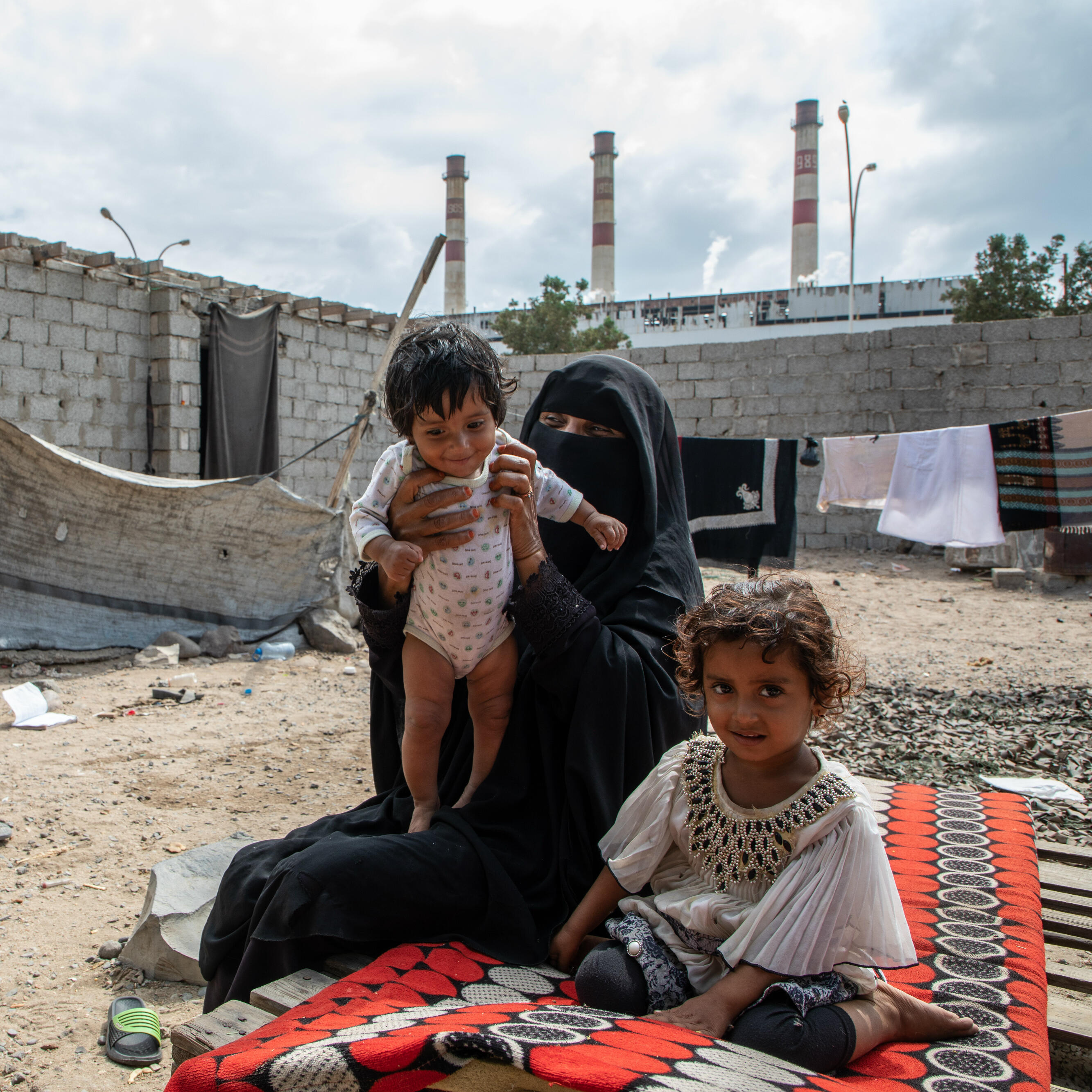 A mother and her two young children seated outdoors in Yemen