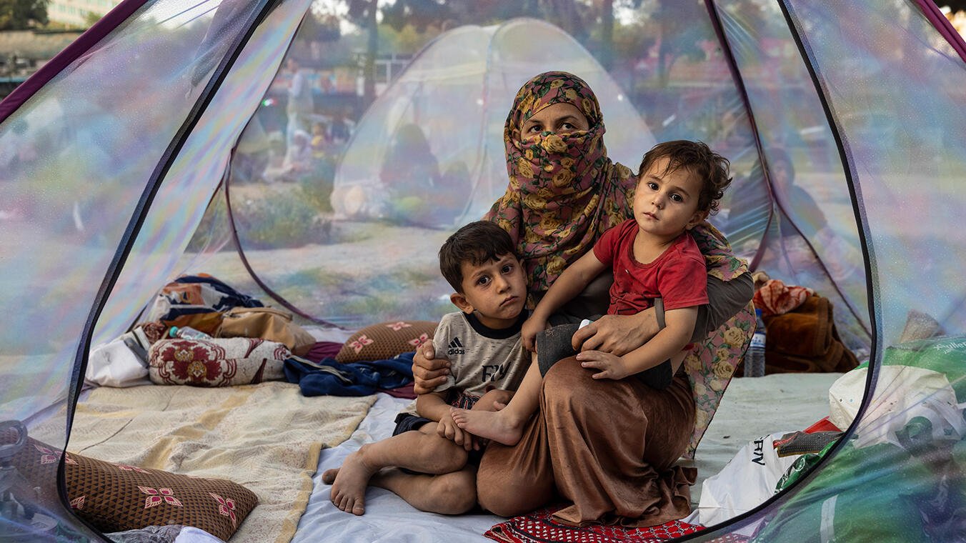 A mum with two young children sit in a tent 