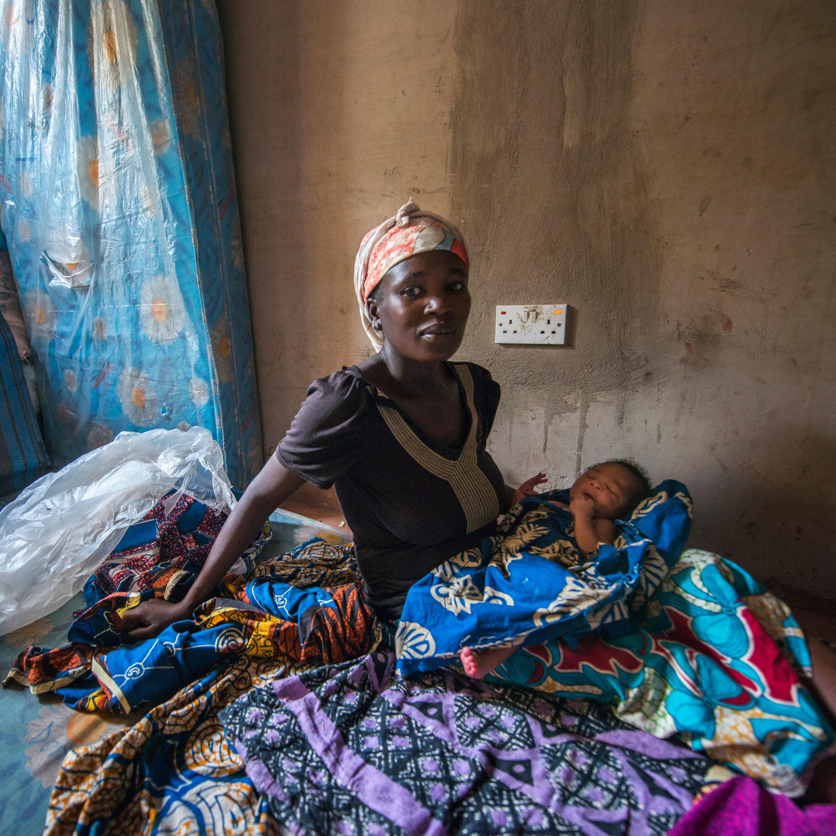 A Nigerian woman sits on a mattress with her infant child.