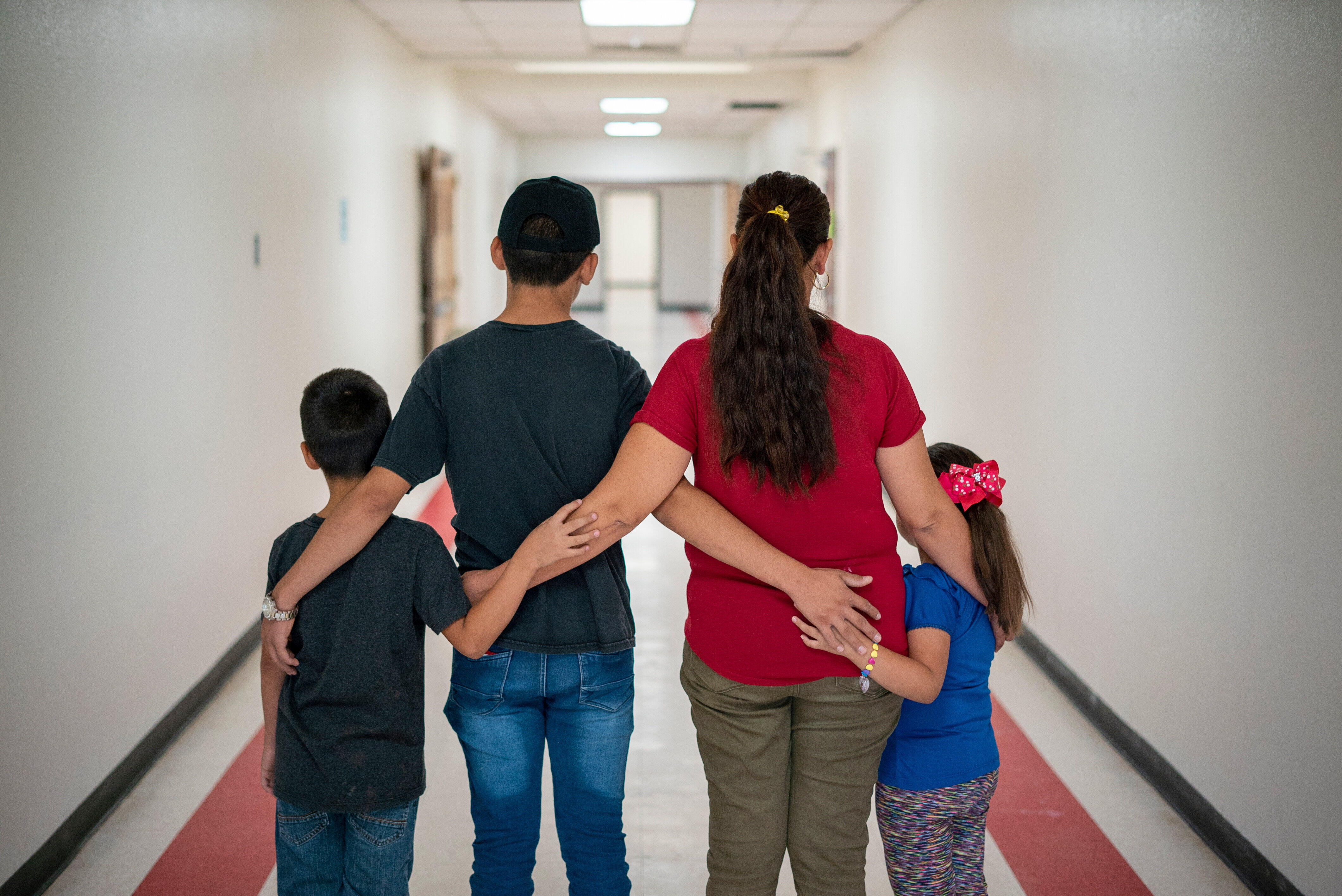 Luisa, an asylum seeker from Mexico, stands with with her children in Arizona after she was able to cross the US border. They are standing in a hallway with their backs to the camera, to protect their identities. 