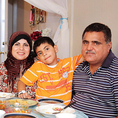 A father, mother and young son sit at a kitchen table. 