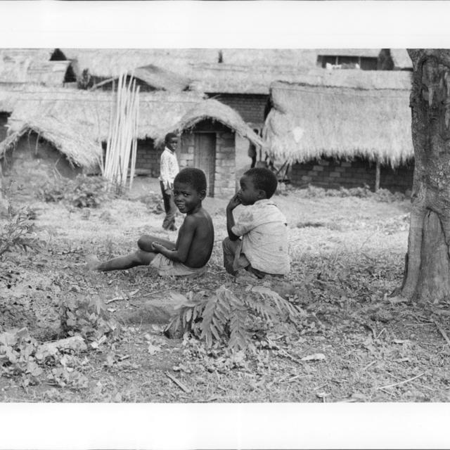 Des enfants réfugiés angolais sont assis par terre devant une rangée de maisons au Zaïre.