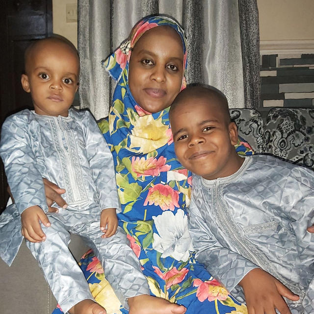 Dr Fatima Ibrahim Lawan, a mother and roving nutrition manager in Nigeria, with her children. Dr Fatima Ibrahim Lawan poses with her children on either side of her as she sits on a couch.