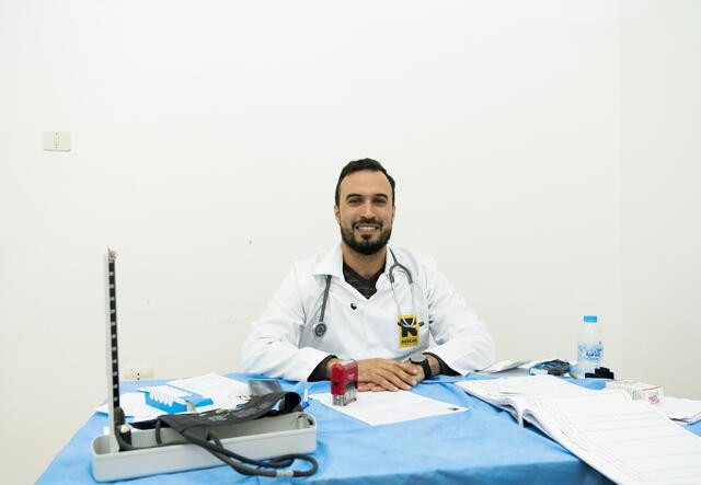 A man sits smilingly behind a desk