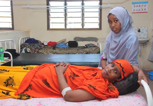 A woman lying on bed in a clinc, behind her a young girl.