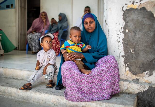 A mother with her two children sitting in front of a house