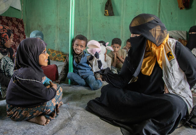 Girl plays with puppet held by IRC community health worker