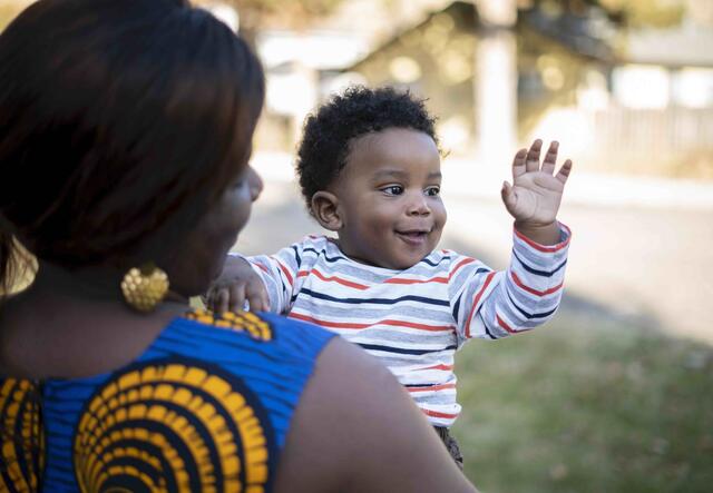 Jaqueline, an interpreter, holds her baby who is waving outside their home