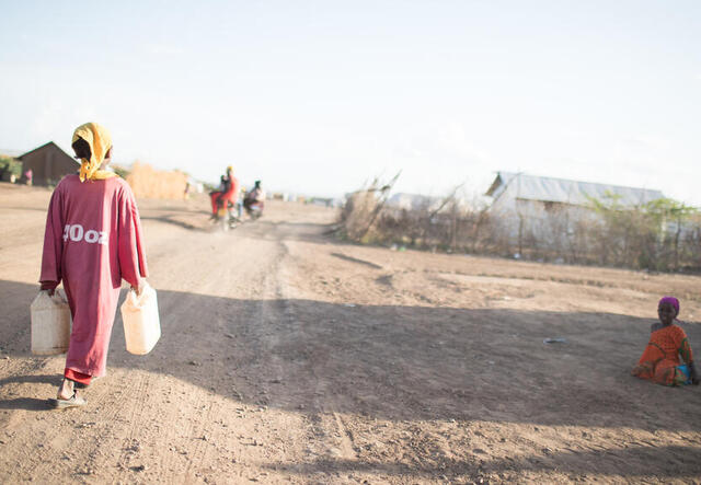 A 10-year-old girl carries two water jugs as she walks through a parched landscape near a refugee camp in Kenya.