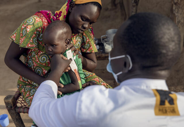 MUAC tape is used to identify whether a child may be malnourished. The tape, similar to a sewing measuring tape, is used to measure the circumference of a child’s mid-upper arm. If the score indicates malnourishment, the IRC teams refer the child for further treatment. Here an IRC care provider fits the MUAC tape to a Sudanese boy.