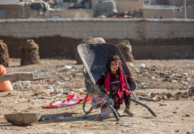 In the Ghaibi Bala camp where the International Rescue Committee (IRC) is conducting a needs assessment of vulnerable families living in the camp in Kabul, Afghanistan to see if they meet the criteria to receive a cash distribution from the IRC., a girl plays in a wheel barrow.