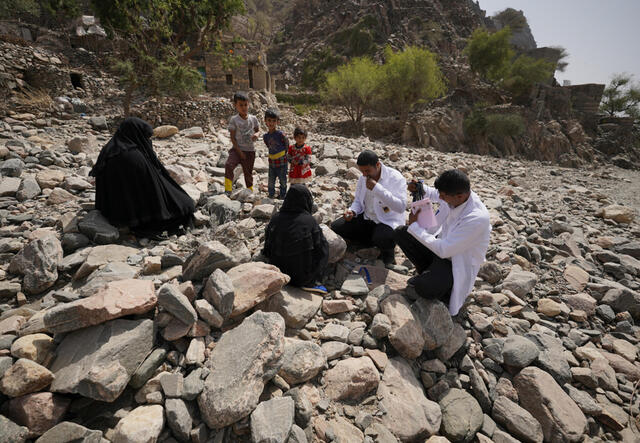 Two doctors in white coats treat two women on rocky terrain