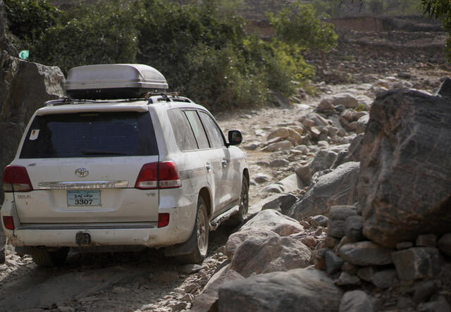 View of white car from the back driving along a rough rocky road