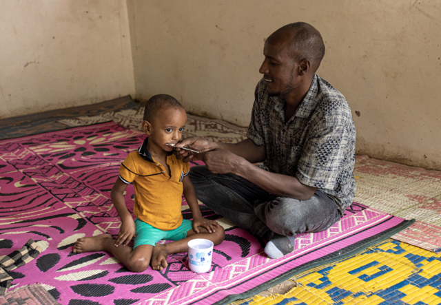 A man feeds his son in a Kenyan refugee camp