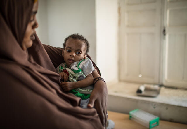 A mother stands holding her malnourished 10-month-old daughter at an IRC clinic in Somalia.