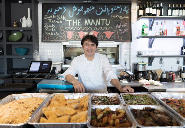 Chef Noori stands smiling with large trays of food in front of him