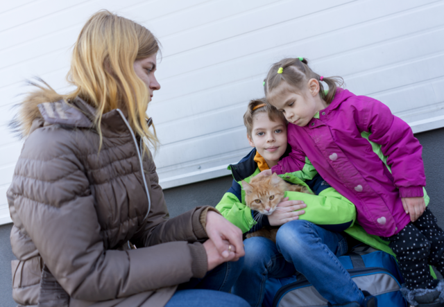 A mother sits with her son, daughter, and their family's cat.