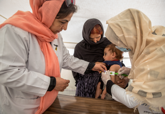 Three women hold a girl who is being screened for signs of malnutrition.