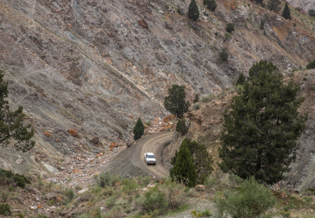 A truck traverses a dirt path in a mountainous setting.