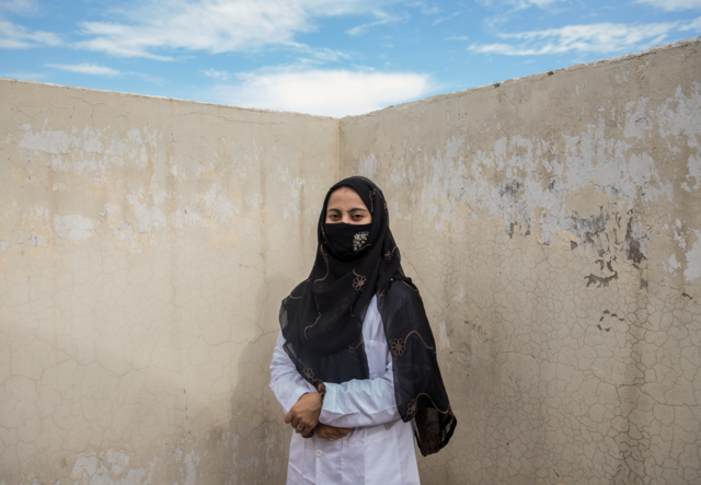 Amna Gul stands against a wall, facing the camera.