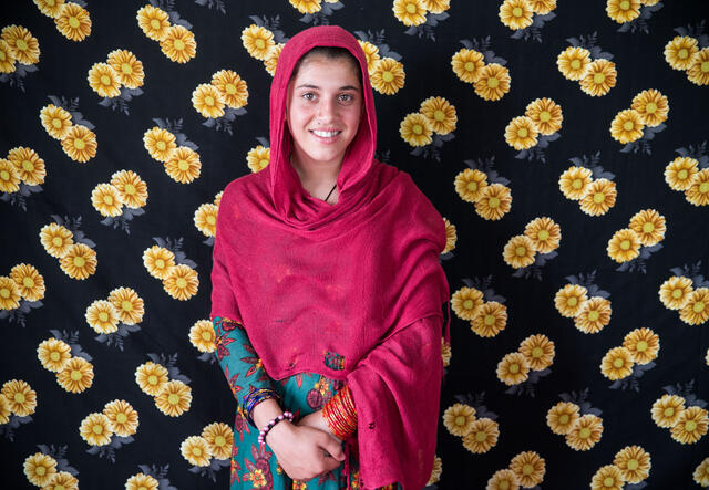 A girl stands in front a wall of flowers