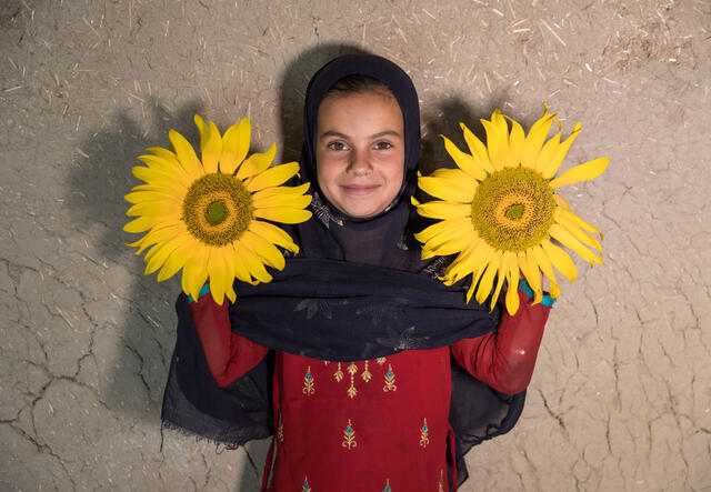 A girl stands holding two sunflowers