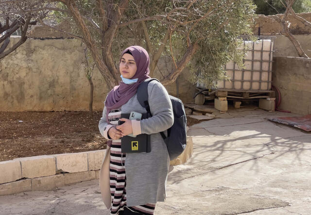Somaya, the IRC Community Mobiliser walking outdoors, holding some books