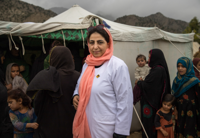 나지아 박사는 텐트와 한 무리의 여성들 앞에 서 있습니다.