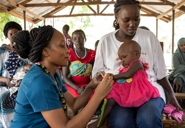 An IRC doctor treats a one year old girl who sits on her mother's lap.