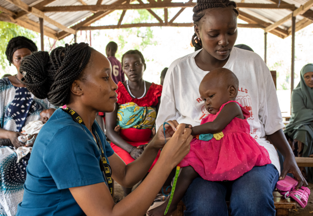 An IRC doctor treats a one year old girl who sits on her mother's lap in a refugee camp in Kenya..