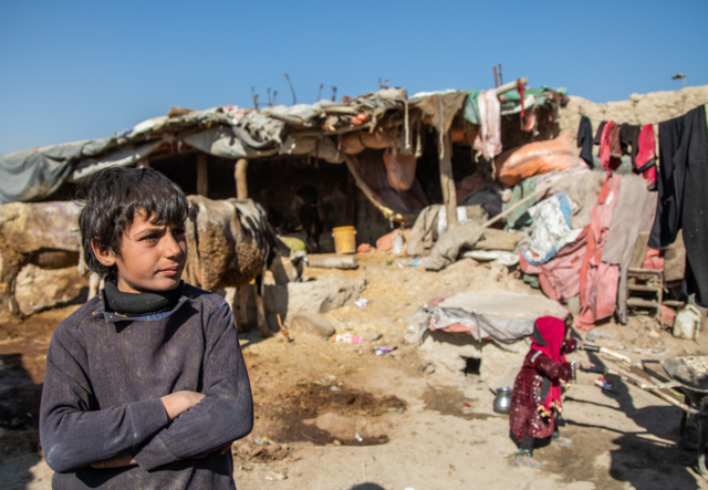 A boy, living in Ghaibi Bala camp in Kabul, Afghanistan, looks on as his mother is interviewed by International Rescue Committee (IRC) staff to see if she meets the criteria to receive a cash distribution from the IRC. The impact of Afghanistan's economic problems is evidenced by the conditions of his surroundings.