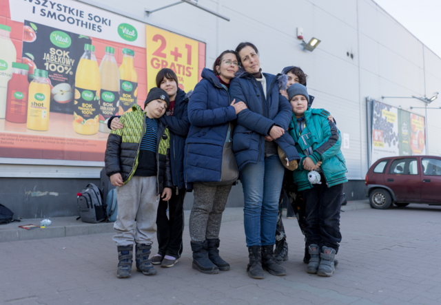 Two sisters stand together in a parklng lot. Each sister has her own two kids with her.