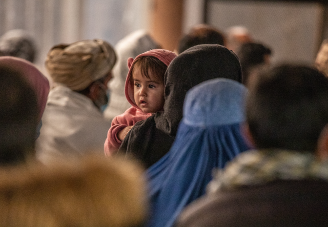 A mother holds a baby in the midst of a crowd of people. They wait to receive IRC cash assistance.