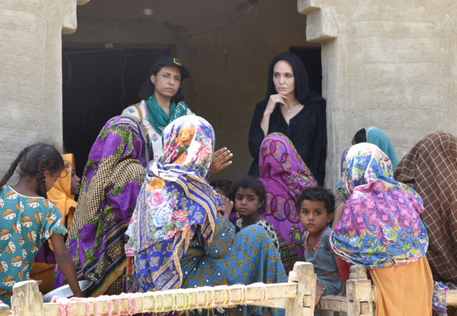 Angelina Jolie visits with women affected by flooding and Pakistan. A few girls look on at the forefront of the picture.