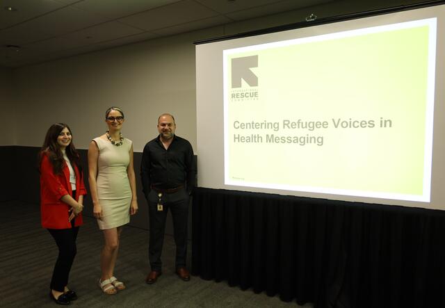 From left to right: (name), (name), and Dr. Omar Aziz stand in front of a projection of the presentation 'Centering Refugee Voices in Health Messaging'