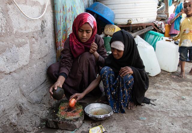 가족을 위한 음식을 만들기 위해 두 소녀가 임시로 만든 조리 장치 앞에서 쪼그리고 앉아 있습니다.
