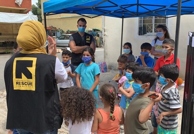 IRC staff members stand with a group of children and deliver psychosocial counseling.