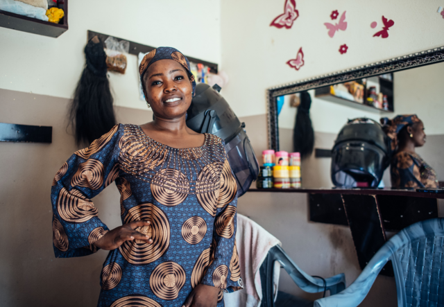 Abigail poses for a portrait in her salon and stands, smiling in front of her salon chair.